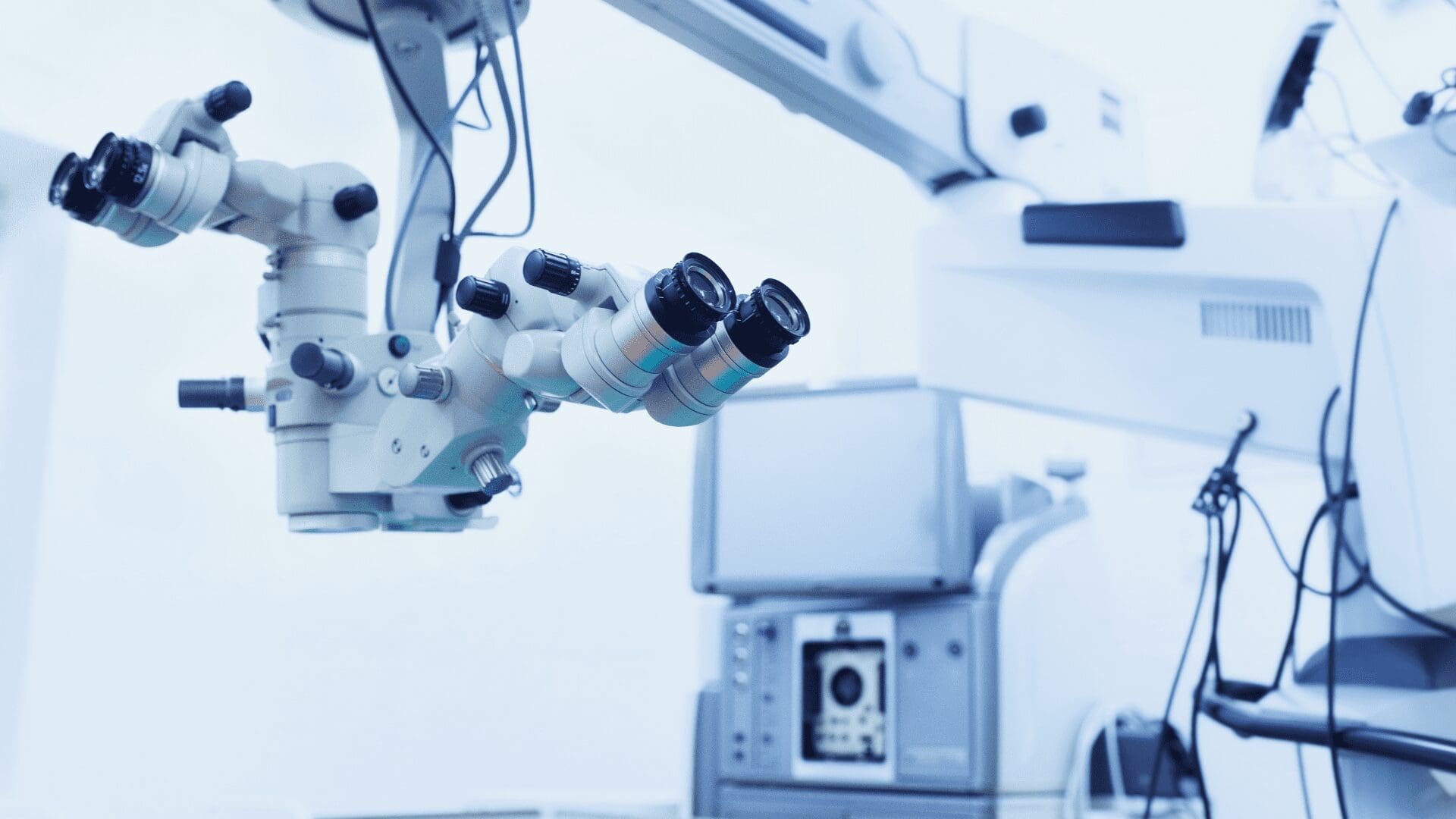 Close-up of a surgical microscope and medical equipment in a modern operating room, with a blue-tinted, sterile environment.